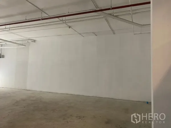 พื้นที่ขายปลีก ให้เช่า - ผนังยาวของยูนิต พร้อมท่อสปริงเกลอร์และระบบต่างๆ บนฝ้าเพดานสีขาว