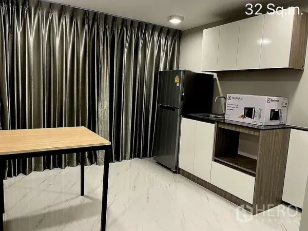 零售空间 出售在Khlong Toei, Bangkok - 紧凑茶水间，白色橱柜、水槽、冰箱和小餐桌，配落地窗帘。