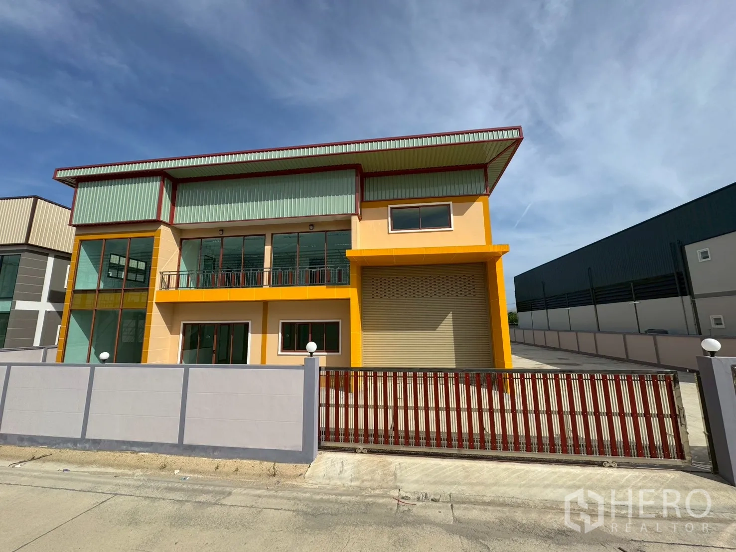 工厂 for sale in Mueang Samut Sakhon, Samut Sakhon - 两层黄色外立面的工厂，带阳台与大型卷帘门，前方有大门与围栏。