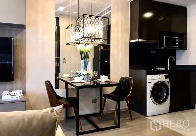 Condominium for rent in Watthana, Bangkok - Dining table set for two beneath pendant lights next to modern kitchen.