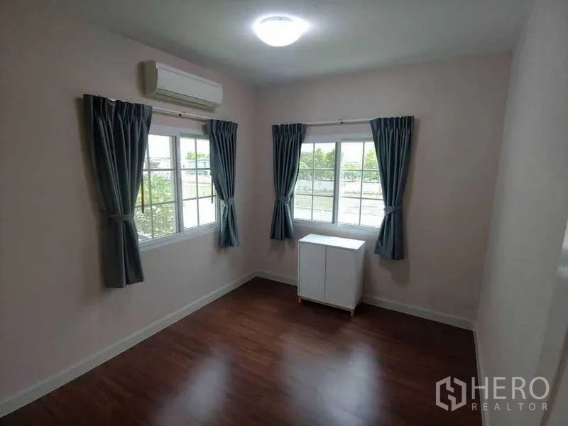 Detached House for sale in Khlong Sam Wa, Bangkok - Bright corner bedroom with wooden floor, two windows, blue curtains, and air conditioner.
