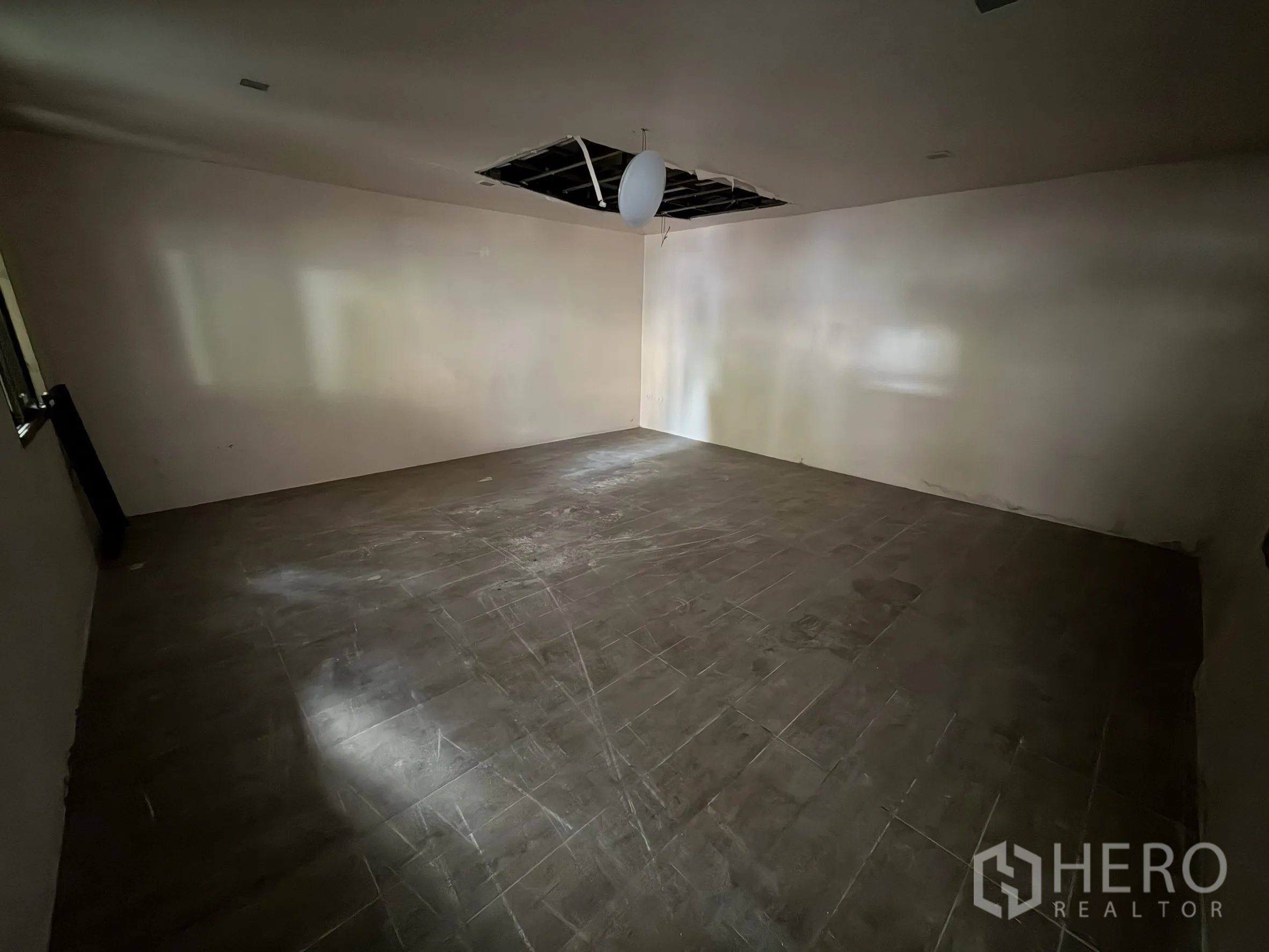 Shophouse for rent in Sathon, Bangkok - Large empty room with grey floor tiles and a partially damaged ceiling.