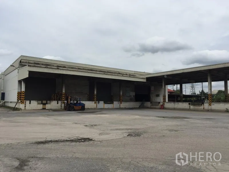 货栈 出租在Pathum Thani - 仓库外观，多个装卸月台与带顶平台，宽阔硬化场地便于大型卡车调头。