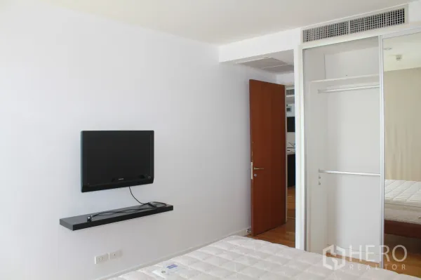 公寓 出租在Sathon, Bangkok - 极简卧室，挂壁电视与镜面移门衣柜，旁有床铺。