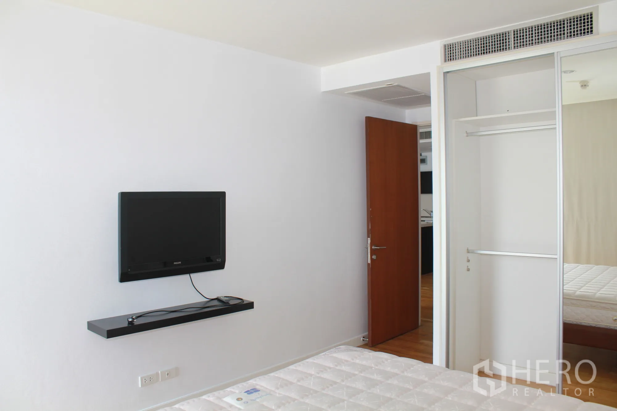 公寓 出租在Sathon, Bangkok - 极简卧室，挂壁电视与镜面移门衣柜，旁有床铺。