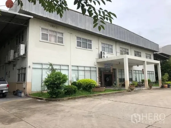 工厂 出租或出售在Lam Luk Ka, Pathum Thani - 办公楼立面近景，带雨棚入口、窗户与绿化。