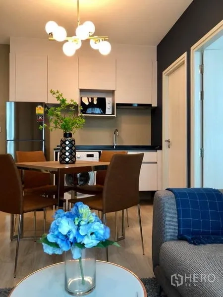 Condominium for rent or sale in Huai Khwang, Bangkok - Compact kitchen with white cabinetry and microwave, four-seat dining set, and sofa in an open-plan layout.