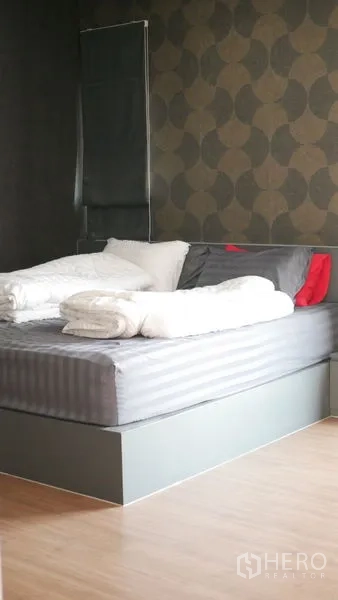 Detached House for rent or sale in Bang Bo, Samut Prakan - Primary bedroom with patterned accent wall, platform bed and wood flooring.