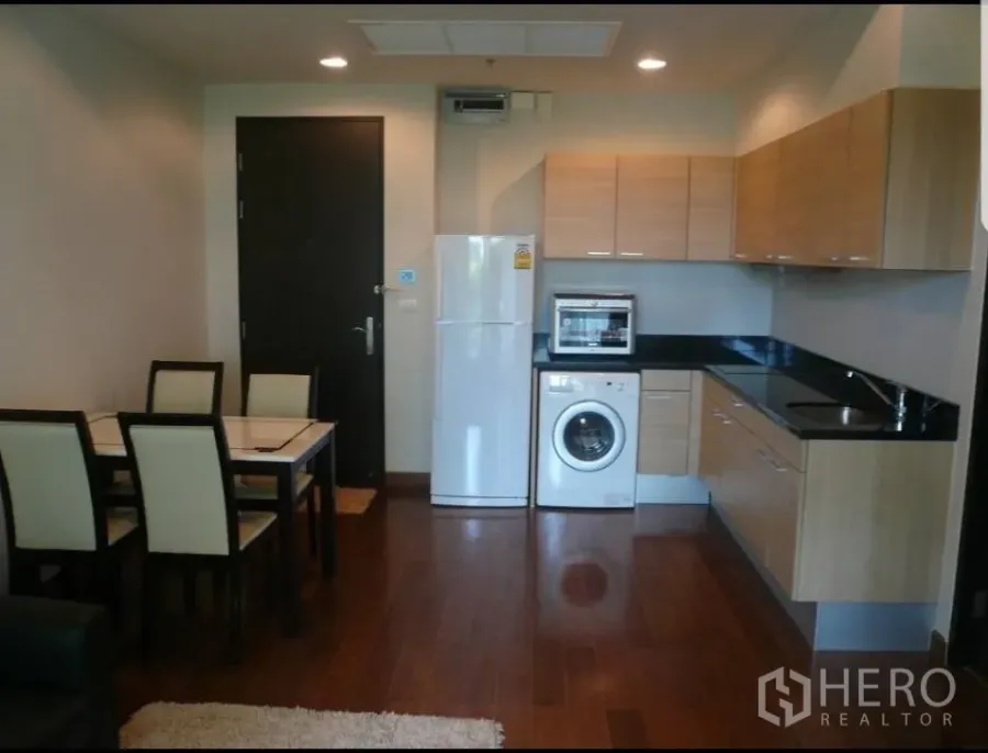 公寓 出租在Pathum Wan, Bangkok - 开放式厨房，木质橱柜与黑色台面，配冰箱、洗衣机与餐桌，木地板。