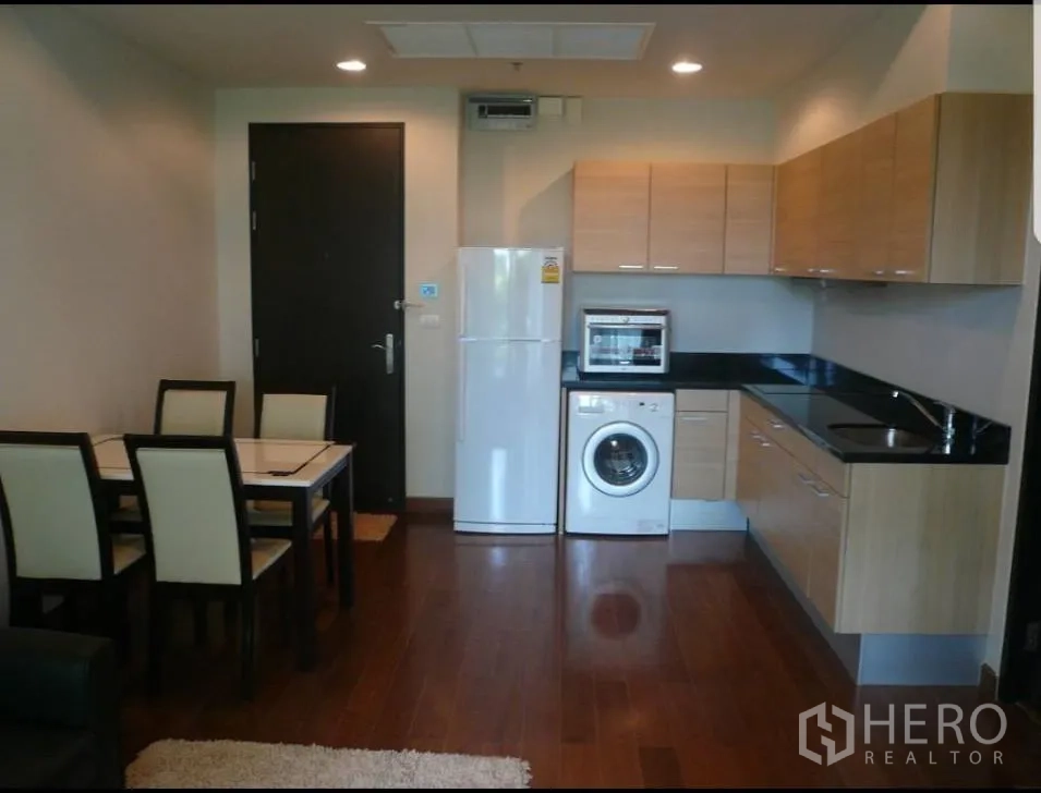 公寓 出租在Pathum Wan, Bangkok - 开放式厨房，木质橱柜与黑色台面，配冰箱、洗衣机与餐桌，木地板。