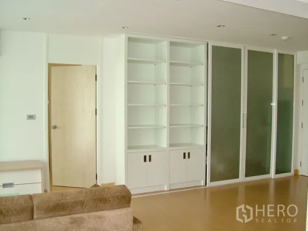 Condominium for rent or sale in Khlong Toei, Bangkok - Bright living area with built-in white shelving, sliding glass doors and light wood floors.
