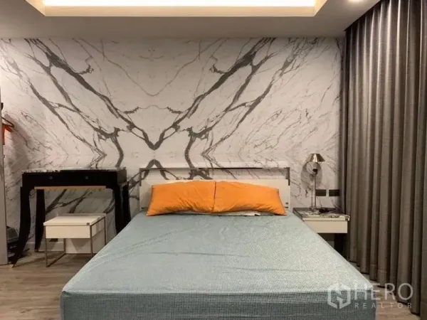 คอนโด ขายในKhlong Toei, Bangkok - ห้องนอนผนังลายหินอ่อน เตียงหุ้มผ้า หมอนสีส้ม โต๊ะข้างเตียง และผ้าม่านทึบแสง