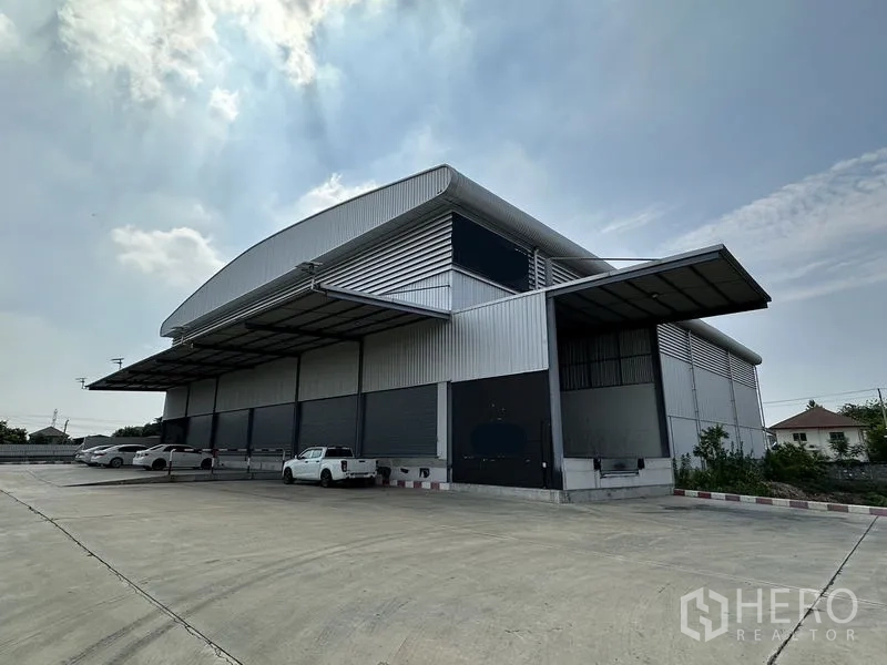 Warehouse for rent in Lat Krabang, Bangkok - Modern steel warehouse exterior in Lat Krabang with wide covered loading bays, multiple roller shutters and a large concrete yard for truck access.
