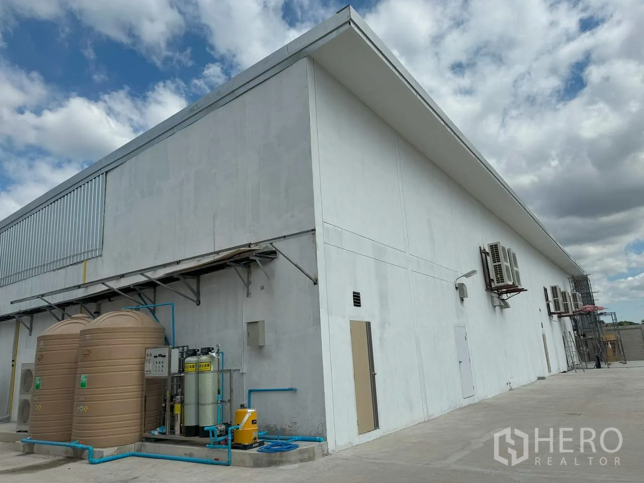 Warehouse for rent in Mueang Pathum Thani, Pathum Thani - Exterior of the warehouse with water tanks, filtration system, air-conditioning units, and paved yard.