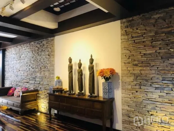 Condominium for rent in Pathum Wan, Bangkok - Hallway with console table and Thai-style statues framed by illuminated stone walls and coffered ceiling.