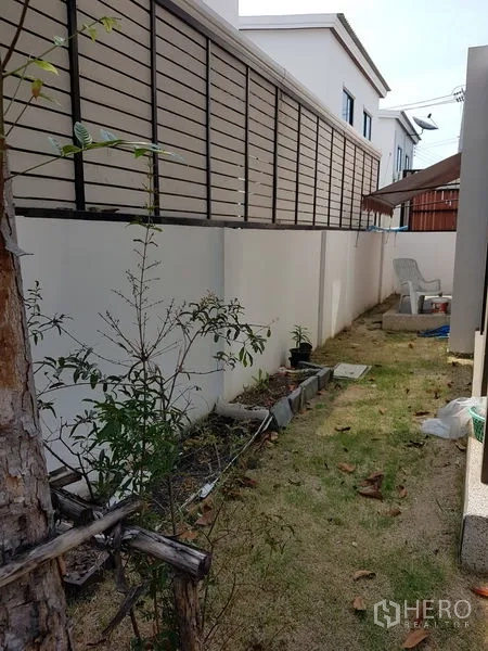 Detached House for sale in Samut Prakan - Narrow backyard garden with fence, young plants and outdoor seating.