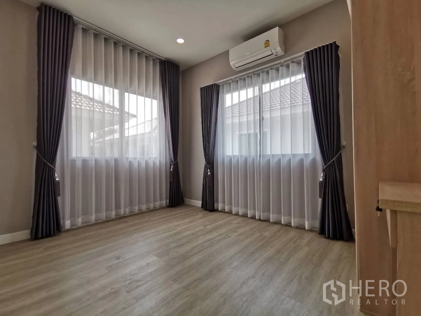 Detached House for rent in Bang Phli, Samut Prakan - Sunlit upstairs room with two large windows, sheer and blackout curtains, wood flooring, and wall-mounted air conditioner.