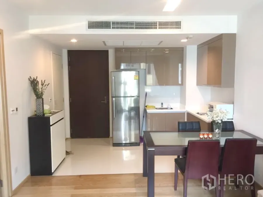 公寓 出租在Khlong Toei, Bangkok - 开放式厨房与餐区，亮面橱柜、不锈钢冰箱与玻璃餐桌，现代化苏坤逸公寓内部。