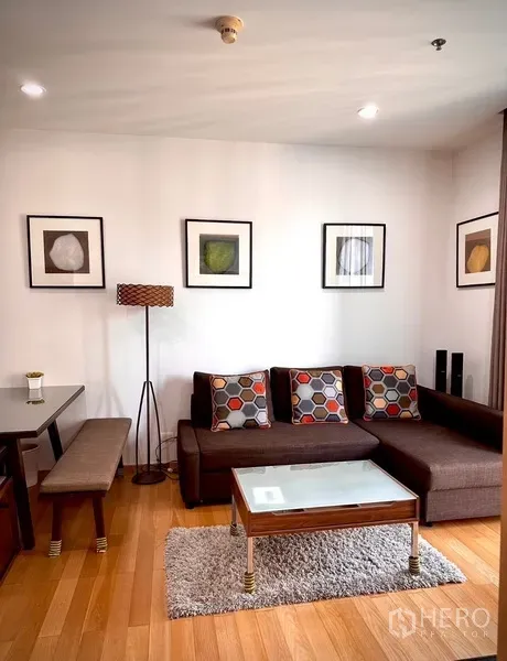 Condominium for rent or sale in Watthana, Bangkok - Close view of L-shaped sofa with patterned cushions, glass coffee table, rug and floor lamp.