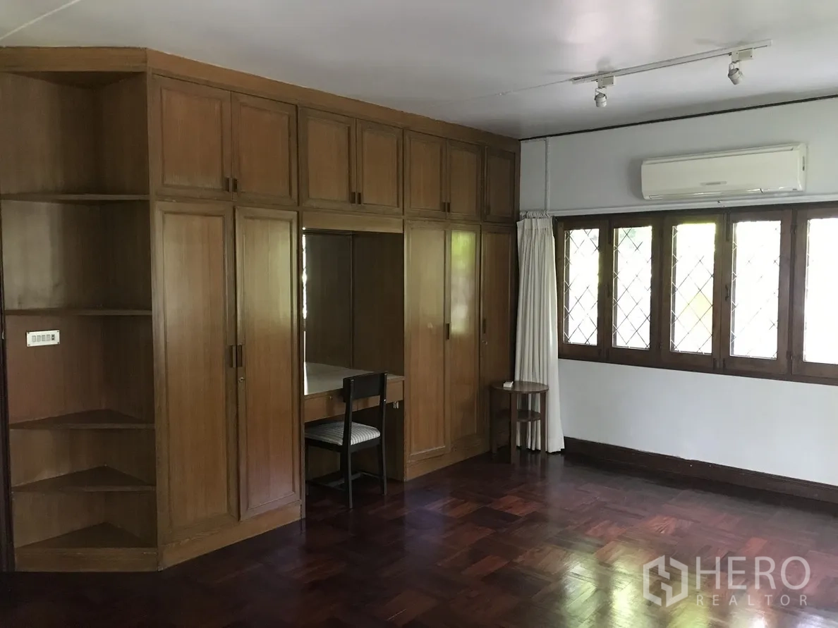 Detached House for rent in Khlong Toei, Bangkok - Bedroom with built-in wooden wardrobes, parquet floor, and air conditioning.