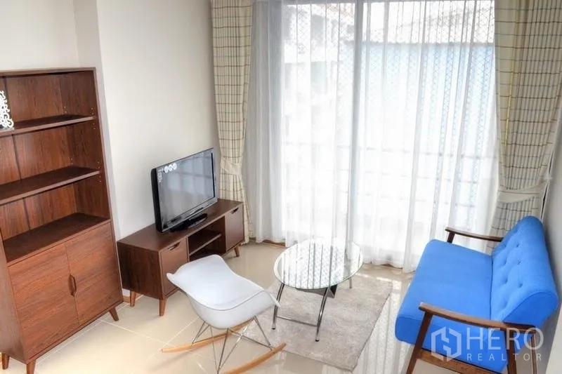 คอนโด ให้เช่าในPhaya Thai, Bangkok - ห้องนั่งเล่นคอนโด 2 ห้องนอน ใกล้ BTS อารีย์ โซฟาสีน้ำเงิน โต๊ะกระจก และประตูกระจกออกระเบียง