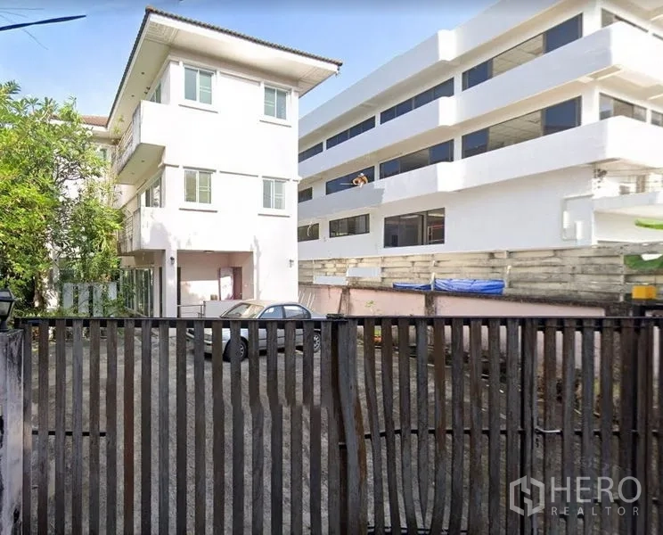 带办公室的家 出售在Phra Khanong, Bangkok - 帕卡侬区域三层白色家办楼外观，带铁门入口与前院停车区，邻近现代建筑。