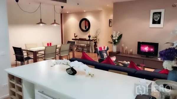 公寓 出租在Bang Rak, Bangkok - 从厨房中岛望向客厅与餐区，暖色灯光与现代装饰。