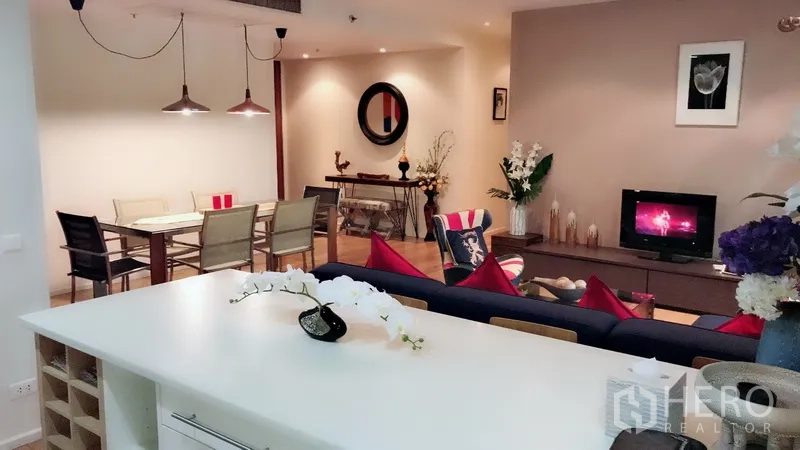 公寓 出租在Bang Rak, Bangkok - 从厨房中岛望向客厅与餐区，暖色灯光与现代装饰。