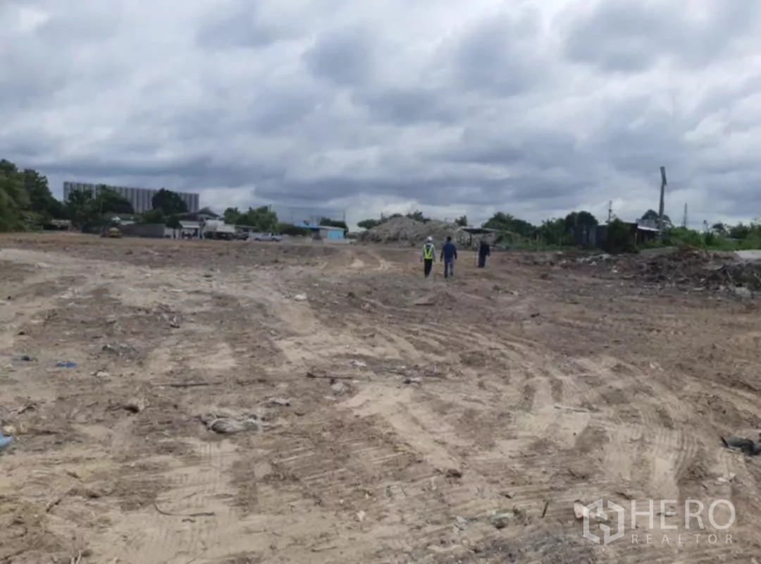Land for sale in Khlong Toei, Bangkok - Expansive leveled earth area with tyre tracks and low-rise buildings beyond.