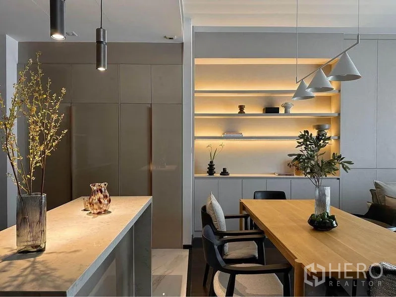 Condominium for rent or sale in Watthana, Bangkok - Dining and living space with backlit shelves, wood table and neutral modern decor.