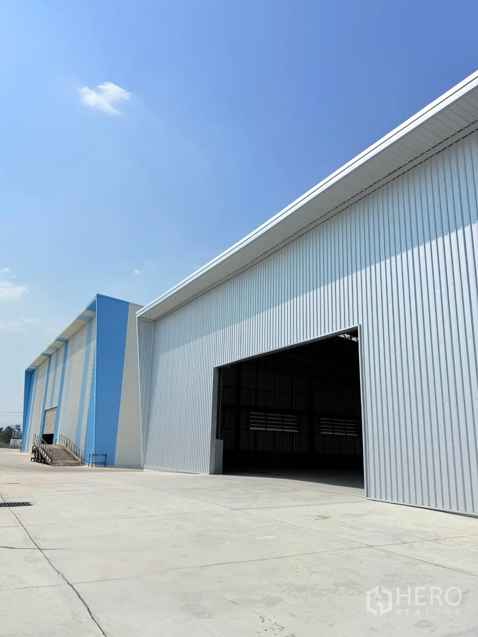 Factory for sale in Ban Bueng, Chon Buri - Row of warehouse buildings with open loading bay and expansive concrete yard under clear sky.