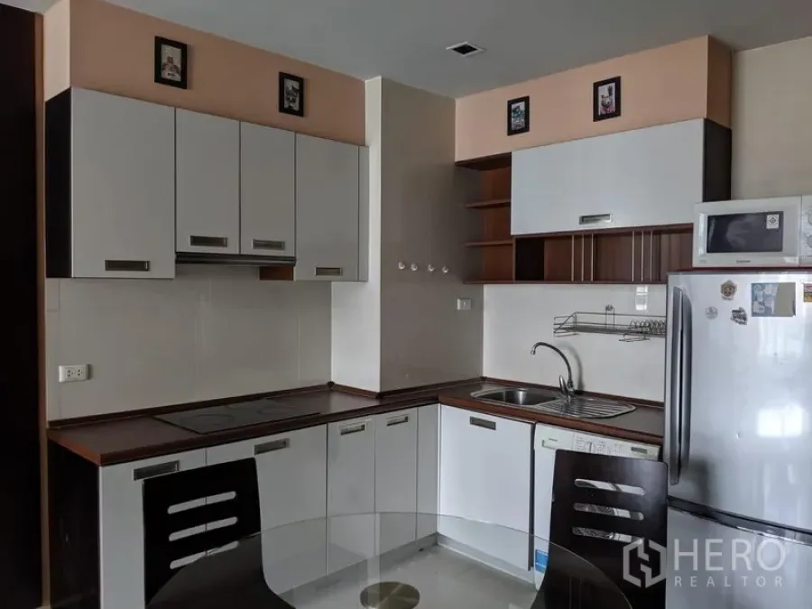 Condominium for rent in Watthana, Bangkok - Modern L-shaped kitchen with white cabinets, cooktop and full-size fridge in a Sukhumvit condominium.