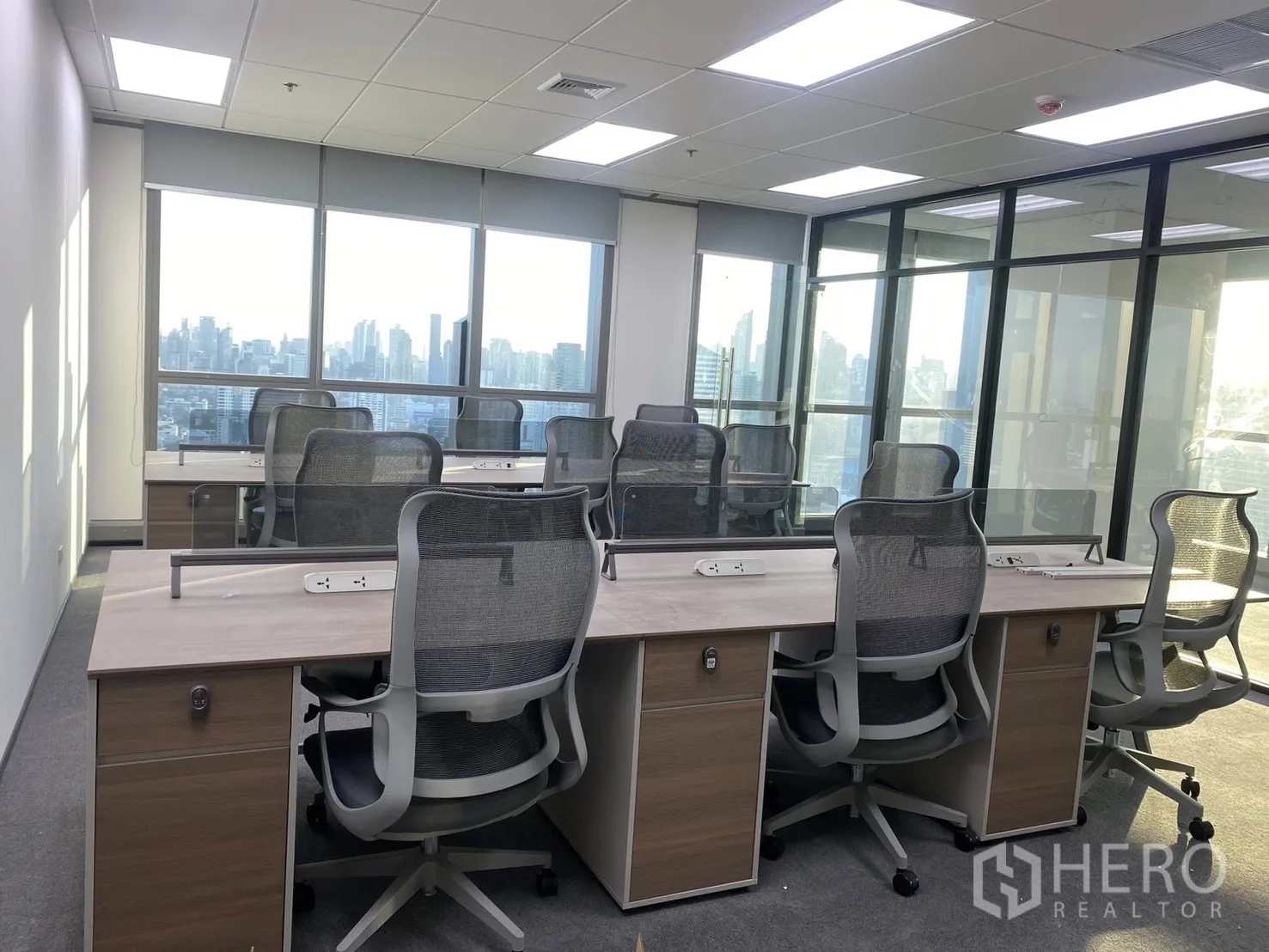 สำนักงาน for rent in Huai Khwang, Bangkok - โต๊ะแบบเบนช์พร้อมเก้าอี้ตาข่าย ช่องปลั๊กไฟ และหน้าต่างบานใหญ่เห็นวิวสกายไลน์