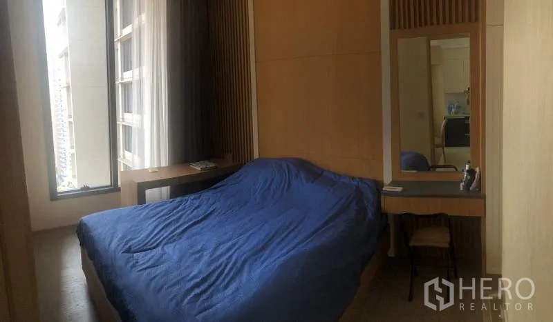 Condominium for rent or sale in Watthana, Bangkok - Cozy second bedroom with desk, mirror and floor-to-ceiling window overlooking city buildings.