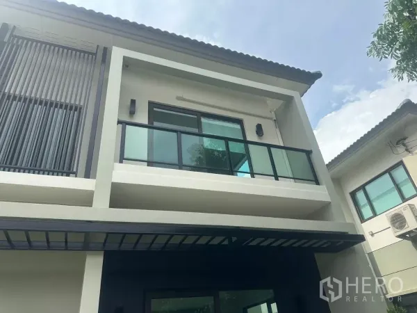 Detached House for sale in Samut Prakan - Close-up of the upper facade showing a glass balcony and vertical privacy slats under the eaves.