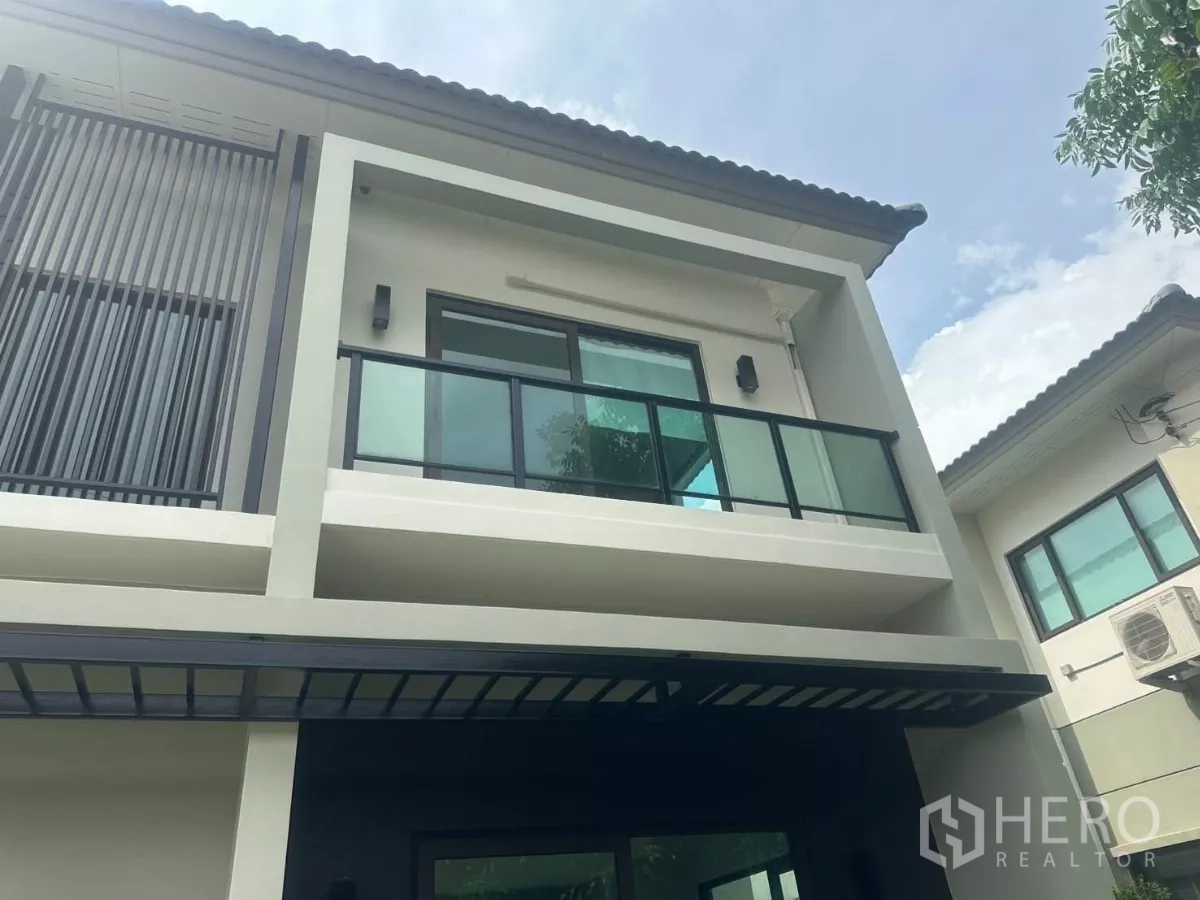 Detached House for sale in Samut Prakan - Close-up of the upper facade showing a glass balcony and vertical privacy slats under the eaves.