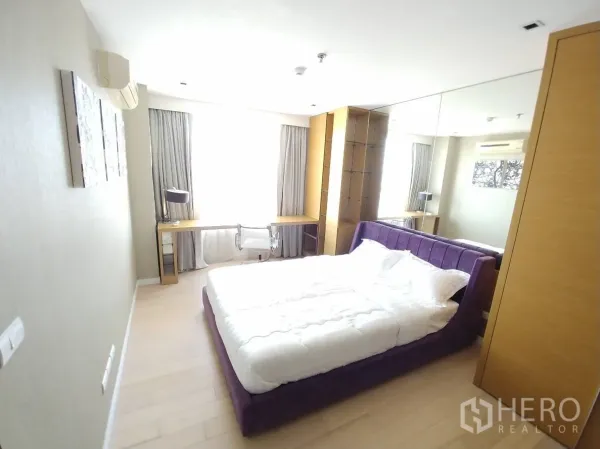 公寓 出租在Watthana, Bangkok - 次卧配紫色软包床、大镜面衣柜与窗边长书桌。