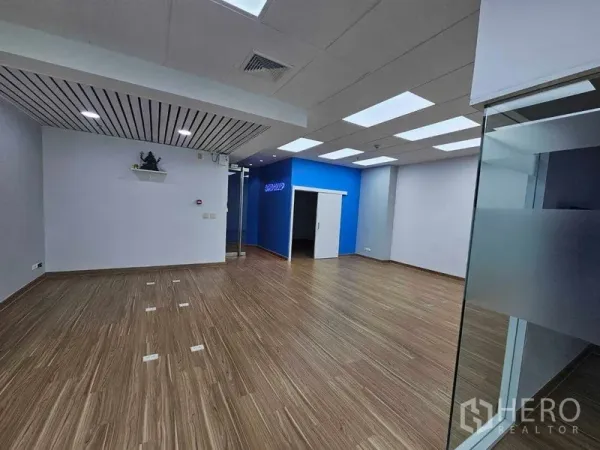 Office Space for rent in Sathon, Bangkok - Open-plan office with wood floors, LED panel ceiling, blue accent wall and glass entry.