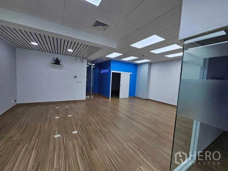 Office Space for rent in Sathon, Bangkok - Open-plan office with wood floors, LED panel ceiling, blue accent wall and glass entry.