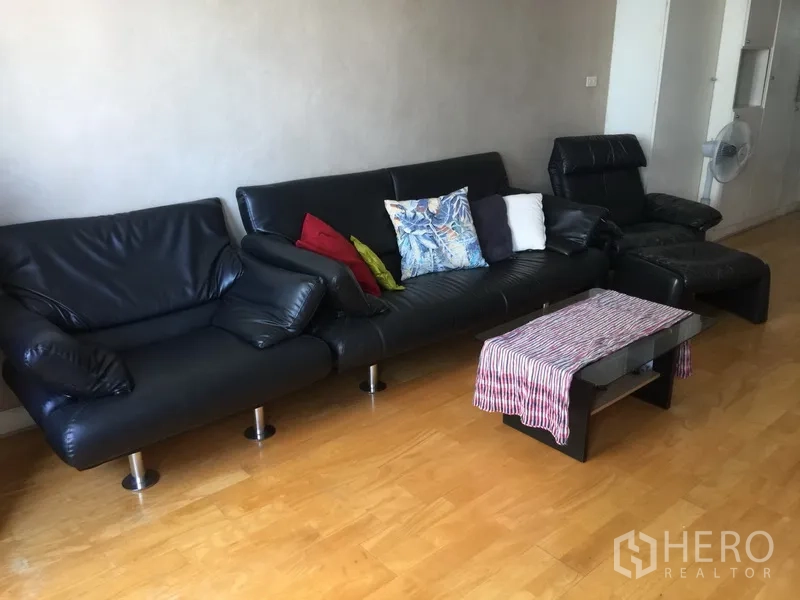 公寓 出租或出售在Watthana, Bangkok - 宽敞客厅，黑色皮沙发与茶几，木地板。