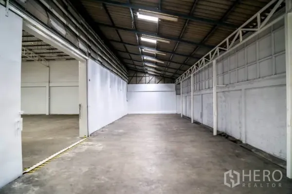 Warehouse for rent in Din Daeng, Bangkok - Long side storage bay with pitched metal roof, white walls and concrete floor connected to the main warehouse.