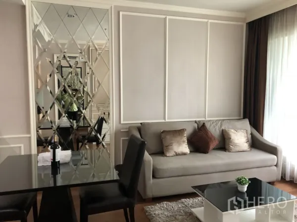 公寓 出租在Pathum Wan, Bangkok - 采光良好的客厅，灰色沙发、菱形镜面墙、餐桌与纱帘。