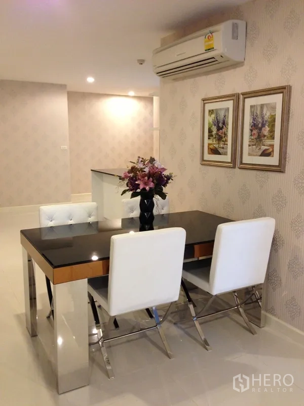 Condominium for rent or sale in Watthana, Bangkok - Dining area with four white chairs, glossy table, air conditioner, and framed art in a Bangkok condominium.