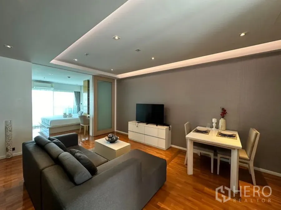 อพาร์ทเมนท์ ให้เช่าในKhlong Toei, Bangkok - ห้องนั่งเล่นและทานอาหารแบบโอเพ่นสเปซ โซฟาสีเทา ตู้วางทีวี และไฟฝ้าซ่อนไฟ