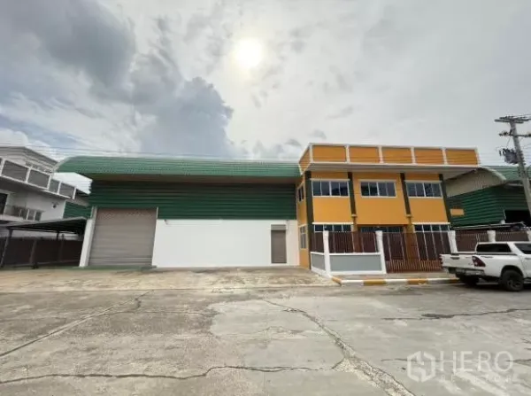 โรงงาน ขายในThanyaburi, Pathum Thani - ภายนอกโรงงานสมัยใหม่ ผนังเมทัลชีทสีเขียว อาคารสำนักงานสองชั้นสีเหลือง พร้อมประตูม้วนและลานคอนกรีตกว้าง