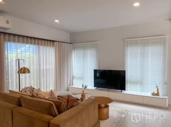 Detached House for rent or sale in Bang Kapi, Bangkok - Cozy lounge with TV console, wide windows with blinds and sheer drapes allowing natural light.