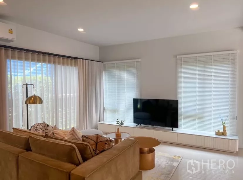 Detached House for rent or sale in Bang Kapi, Bangkok - Cozy lounge with TV console, wide windows with blinds and sheer drapes allowing natural light.