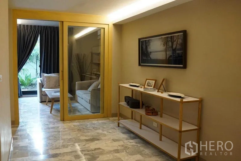 公寓 出租在Watthana, Bangkok - 入口走廊带展示架，玻璃门通向面向花园的休息室。