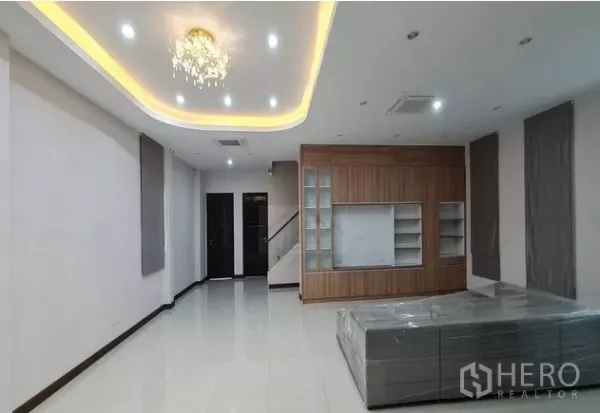 Home Office for rent in Watthana, Bangkok - Bright living area with recessed lighting, chandelier, glossy tile floors, built‑in wall unit and a staircase at the rear.