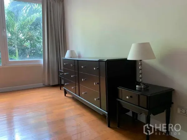 Condominium for rent in Pathum Wan, Bangkok - Bedroom corner with black dresser, bedside table and lamps by the window.